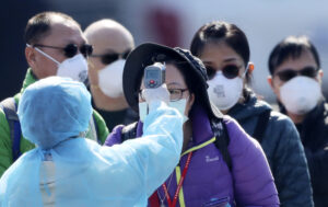 An official in protective suits ensures the temperature of the foreign passengers disembarked from the quarantined Diamond Princess cruise ship before boarding to buses at a port in Yokohama, near Tokyo, Friday, Feb. 21, 2020. Passengers tested negative for COVID-19 started disembarking since Wednesday. (AP Photo/Eugene Hoshiko)